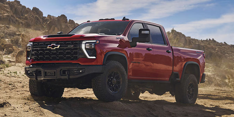 Red Chevrolet Silverado parked on a sandy, desert hill